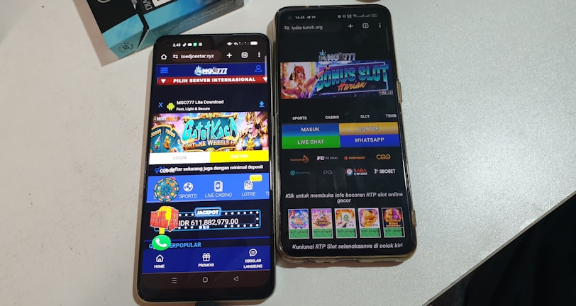 Two smartphones are displayed on a white surface, both showing gambling websites with colorful graphics, text, and various options for logging in and accessing games. The screens are bright and filled with promotional content related to casino and slot games.